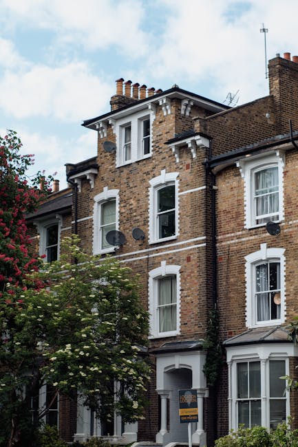 A black and white photograph of a Victorian-era residential building showing two contrasting brick towers with decorative white trim around arched and rectangular windows. The towers are connected by 